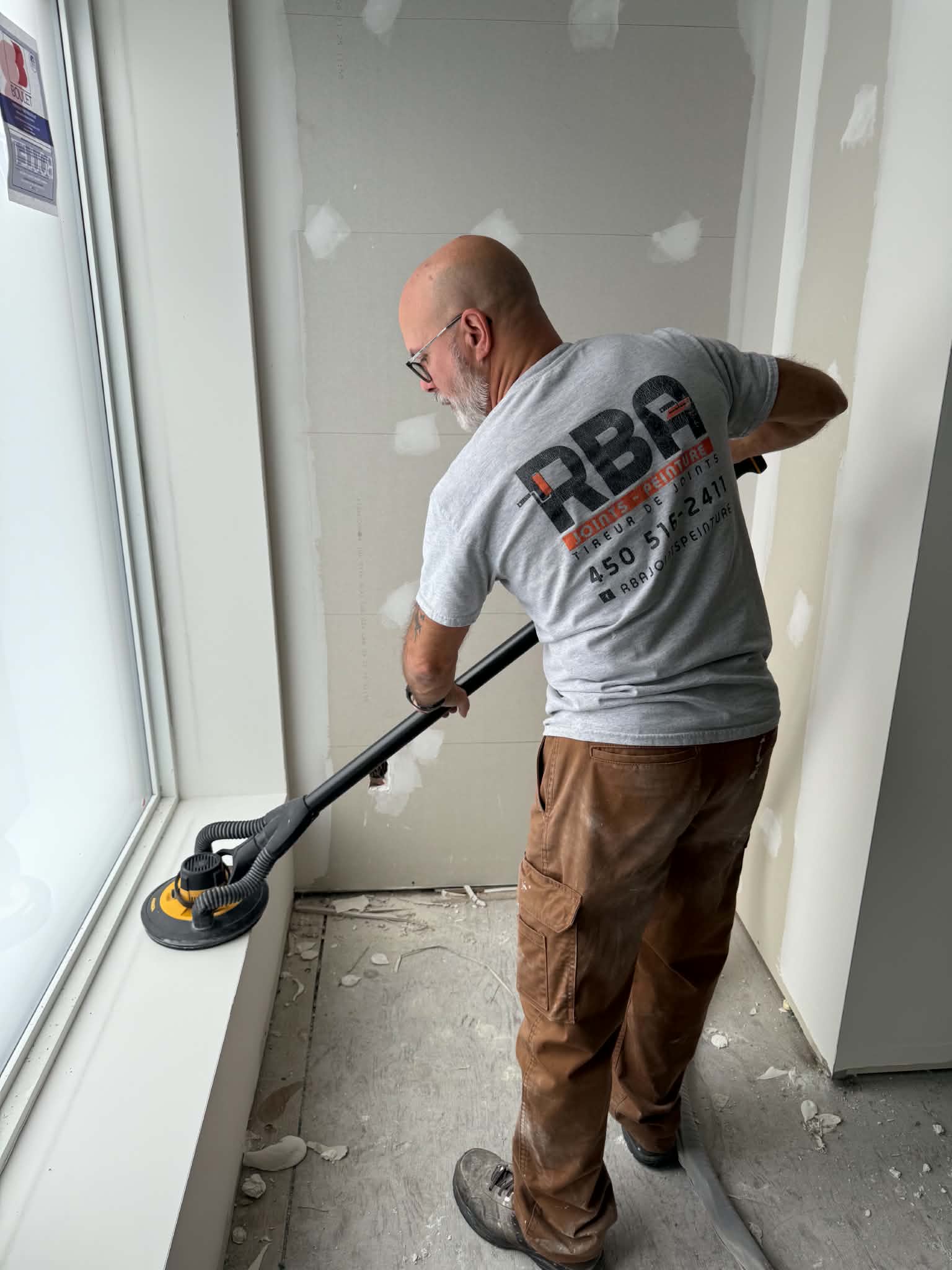 Artisan RBA ponçant un mur de gypse sur un chantier